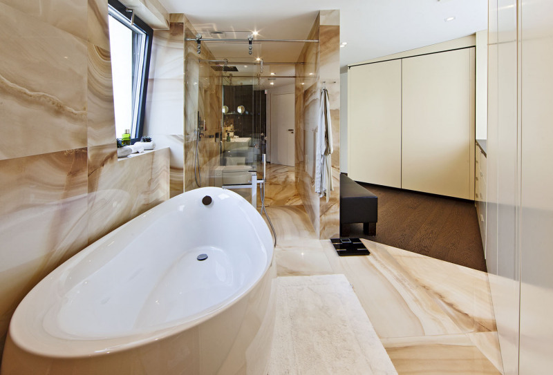 Koupelna rodičů tvoří spolu s šatnou jednolitý prostor, zčásti rozdělený příčkou. Keramické obklady a dlažby značky Porcelanosa dokonale imitují leštěný mramor a dodávají „punc“ luxusu, stejně jako solitérní vana a sanitární vybavení od italského výrobce Gessi